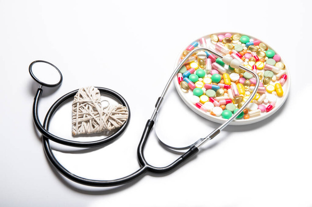 Разноцветные таблетки декоративное сердце и стетоскоп на белом фоне. Лекарство
 - Фото, изображение