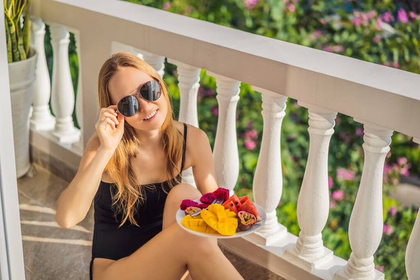 Young woman resting on a balcony with a plate of fruit. life-work balance, relaxation healthy quality living lifestyle in summer holiday vacation of freelancer woman take it easy resting in resort - 写真・画像