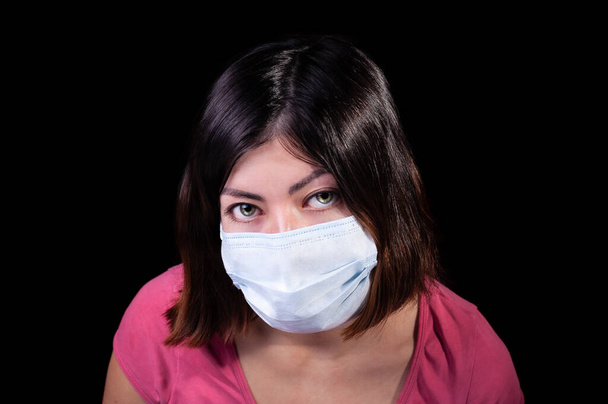 Barna fiatal nő zöld szemekkel fehér eljárással arc maszk egy coronavírus pandémiás fertőzés Covid-19 izolált fekete alapon - Fotó, kép