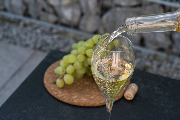 witte wijn in het glas gieten, gezet met druiven op achtergrond - Foto, afbeelding
