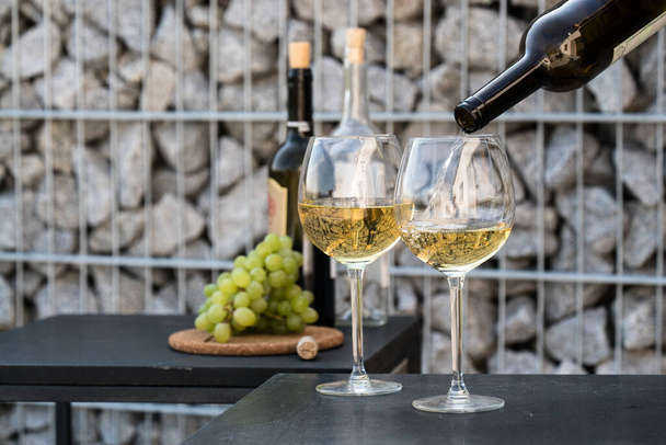 verter vino blanco en las copas, engastado con uvas en el fondo
 - Foto, Imagen