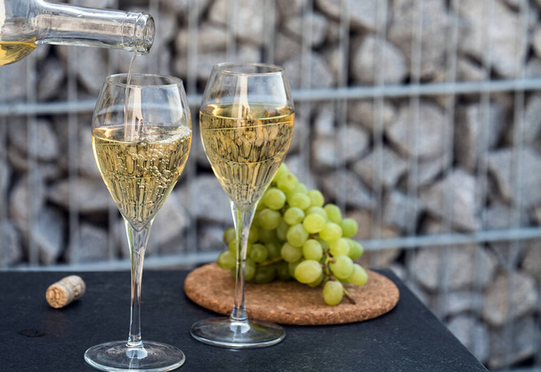 pouring white wine into the glasses, set with grapes on background - Photo, Image