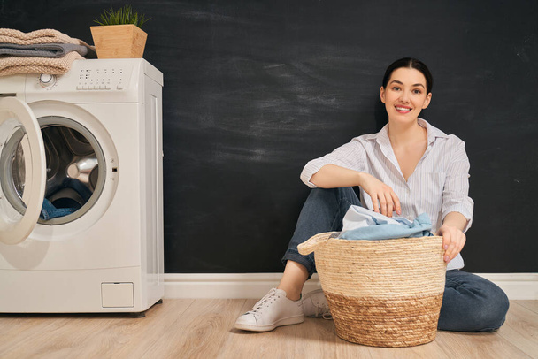 Beautiful young woman is smiling while doing laundry at home.  - Fotografie, Obrázek