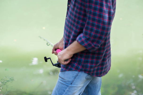 Man fishing at river bank, summer outdoor. Summer leisure, hobby. Fishing. Angling. Man's hand with fishing rod over light green lake water with copyspace. - Foto, Imagem