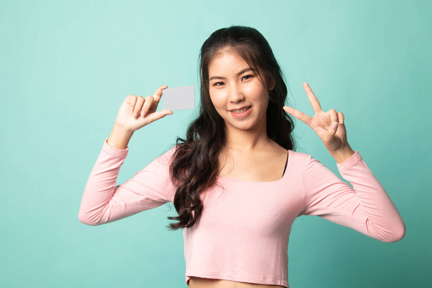 Young Asian woman show Victory with a blank card on cyan background - Valokuva, kuva