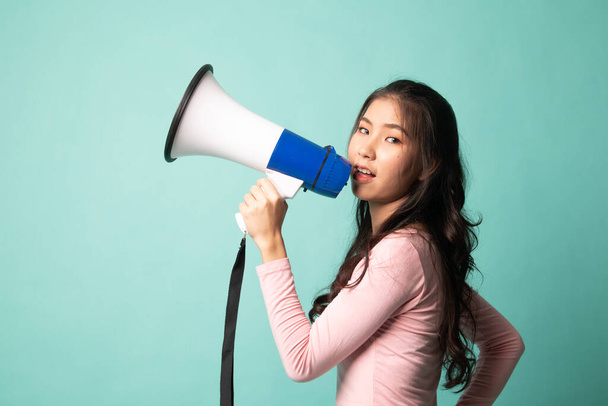 Beautiful young Asian woman announce with megaphone on cyan background - 写真・画像