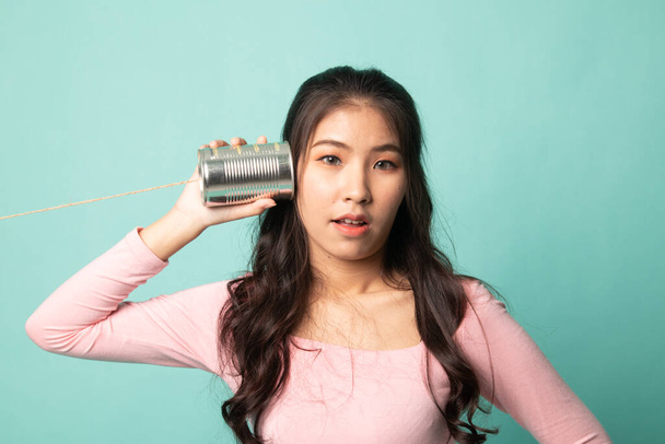 Surprised young Asian woman with tin can phone on cyan background - Foto, Imagen