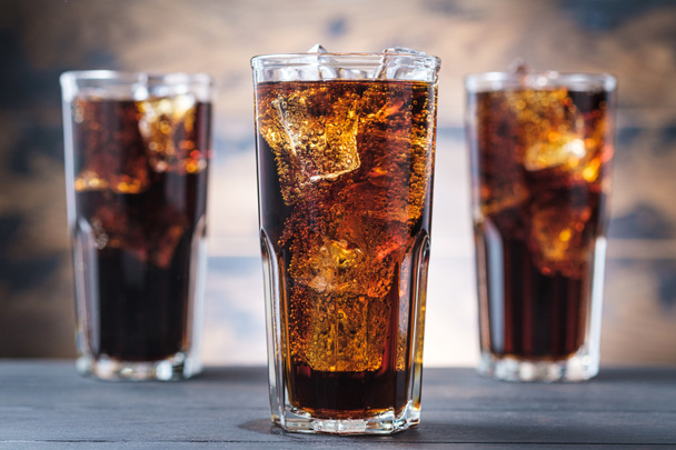 Three cola glass with ice cubes and bubbles. Cold sweet drink on wooden background - Photo, Image