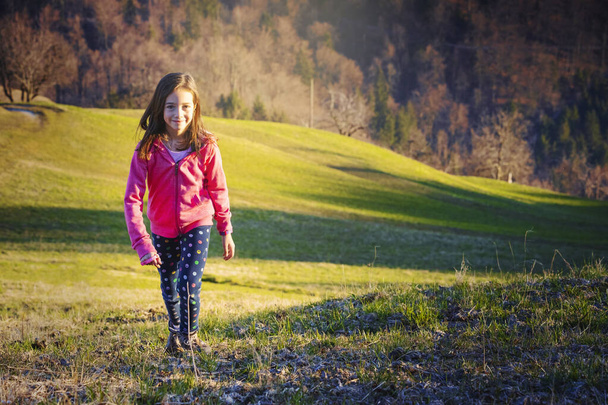 Joven chica activa caminando por los prados verdes. Caminata tardía al atardecer sobre las colinas
. - Foto, Imagen