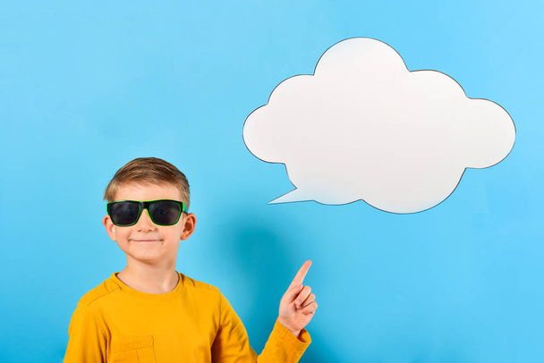 Joyful and smiling boy in glasses shows a finger at a white cloud for text or advertising inscription. - Photo, Image