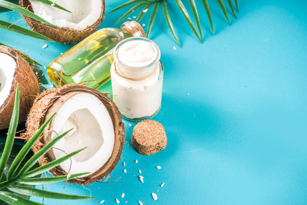 Olej kokosowy w szklanym słoiku z liśćmi tropikalnymi i świeżymi kokosami. Koncepcja olejków organicznych. turkus, tło akwamaryny - Zdjęcie, obraz