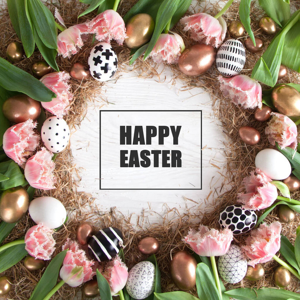 Top view of a round frame with pink tulips with a fringe and golden and black and white Easter eggs lie on the hay. Easter rustic greeting card concept. Copyspace - 写真・画像