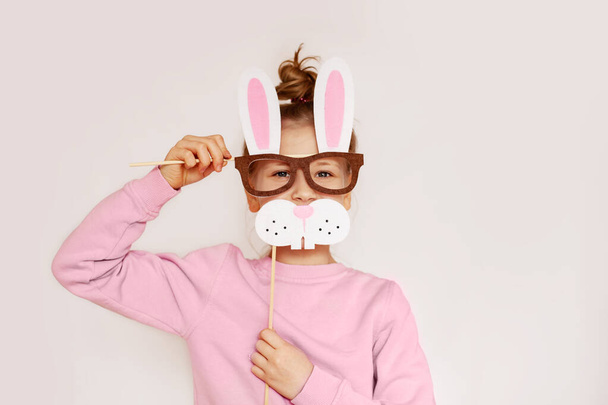 Молода дівчина в масці з кроликовими вухами в рожевому светрі на світлому тлі з простором для тексту. Підготовка до Великодня. Пасхальний костюм кролика. Поняття святкування Великодня - Фото, зображення