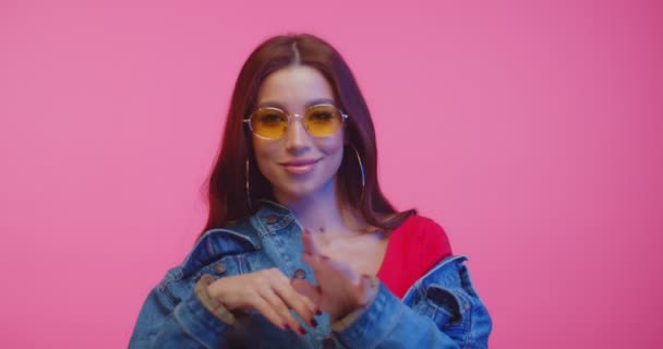 Playful model in yellow sunglasses looking to camera and dancing. Beautifull girl dancing in pink studio. Young woman in sunglasses looking and smiling to camera while dancing on pink background. - Filmati, video