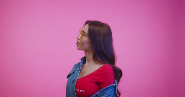 Sassy girl in yellow sunglasses turns around and looks into the camera. Beautiful woman with long brown hair dancing infront of camera. Attractive fashion model in jeans jacket. - Filmati, video