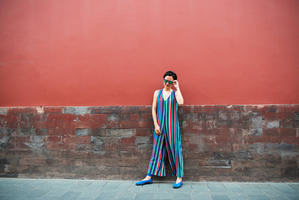 若い魅力的な女性の赤い壁の上に屋外に立って、イメージをトーン。中国の女の子は、夏に楽しませます。美しいアジアのモデルは外で楽しい - 写真・画像