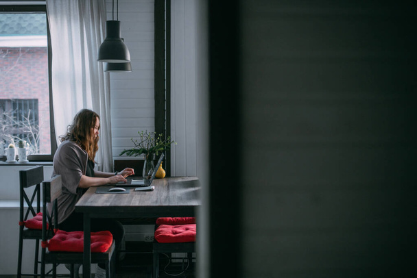 Workplace at home. A woman works on a laptop at home, sits on a sofa in the living room during the day, talks on the phone. Work from home. - 写真・画像
