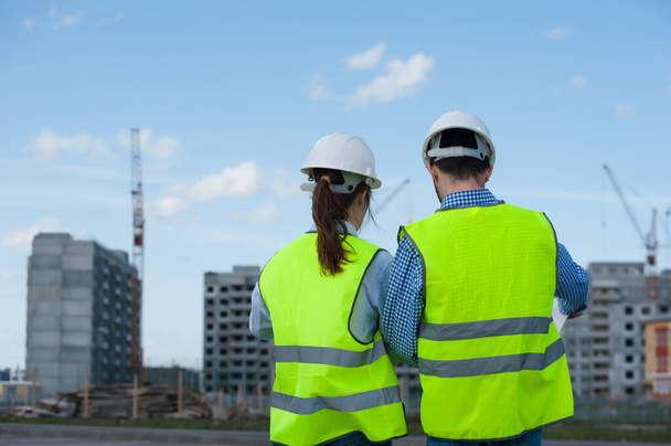 Rear View - Two Young Engineers A Man And A Woman In Green Vests And Helmets Are Discussing A Plan - Fotoğraf, Görsel