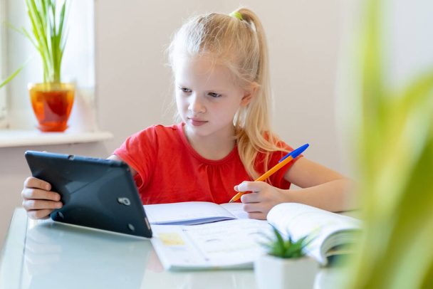 Distance learning online education. Schoolgirl studying at home with digital tablet and doing school homework. Training books and notebooks on table. - Foto, Imagen