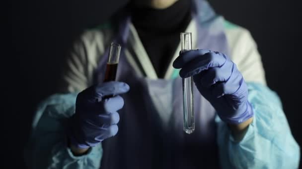 Een close-up van een wetenschapper met glazen mengen oplossingen in bollen. Donkere achtergrond, medisch uniform, overall. - Video