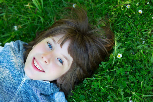 Handsome happy smiling young boy lying on summer meadow green grass with daisy. Attractive smiling teen boy posing over nature background - Photo, Image