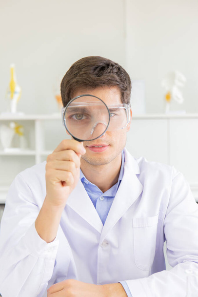 The male doctor looking through the magnifying glass in the lab - Photo, Image