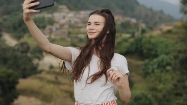 Une jeune caucasienne mince avec de longs cheveux bruns prenant un selfie sur un sommet d'une montagne, colline au Népal. Paysage
. - Séquence, vidéo