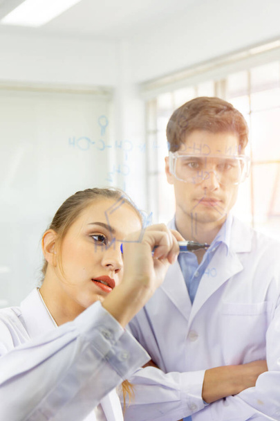 Close-up, a group of scientists, young women and young men are recording formulas on a glass board and have a beautiful orange light. - 写真・画像