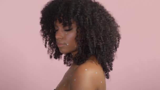 Schwarze Frau mit lockigem Haar und Kristall-Make-up auf rosa Hintergrund im Studio - Filmmaterial, Video