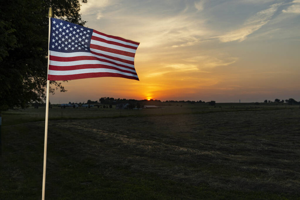 Bandiera amaricana sulla recinzione di una fattoria vicino alla città di Commercio nello Stato dell'Oklahoma, al tramonto, USA
. - Foto, immagini