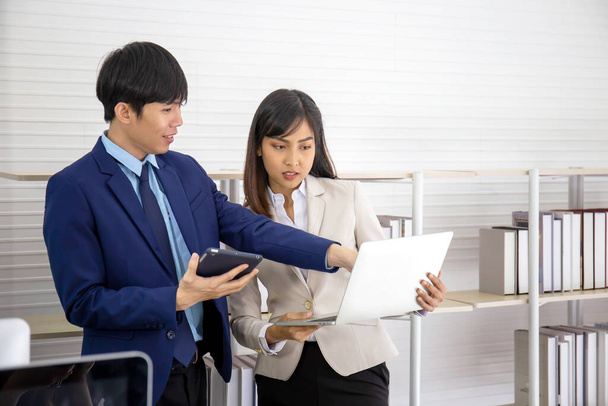 Two young Asian businessmen stand meeting in the office in the hand of the tablet. - Photo, Image