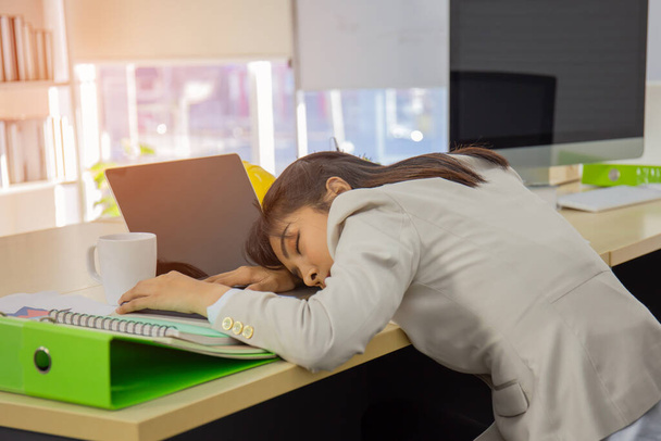 Młoda azjatycka bizneswoman śpi na biurku. - Zdjęcie, obraz