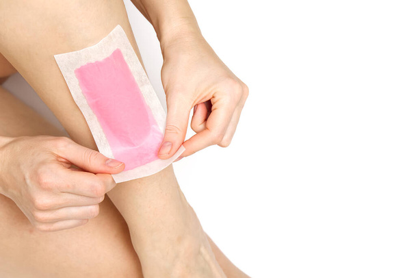 Kobieta używająca różowych pasków wosku. Piękna kobieta depilacja nóg woskiem, odizolowana na biało - Zdjęcie, obraz