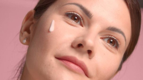 30s brunette woman watching aside with a drop of facial treatment cosmetics on her cheek  - Fotoğraf, Görsel