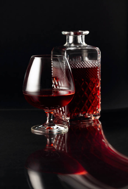 Una copa de brandy y una jarra sobre un fondo oscuro. Reflexión elegante sobre un fondo negro reflexivo
. - Foto, Imagen