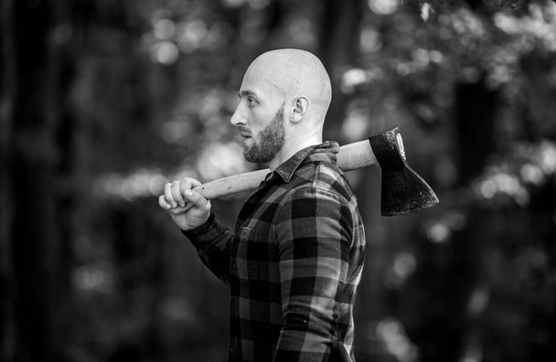 bald woodsman worker. live on rancho. concept of masculinity. bearded hipster cut tree. man checkered shirt use axe. brutal and attractive male in forest. power and strength. lumberjack carry ax - Foto, afbeelding