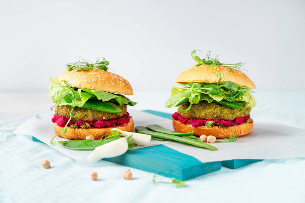 Twee zelfgemaakte veganistische hamburgers met kikkererwtenpattie, groene erwten en rode biet hummus op witte achtergrond. Horizontaal beeld - Foto, afbeelding