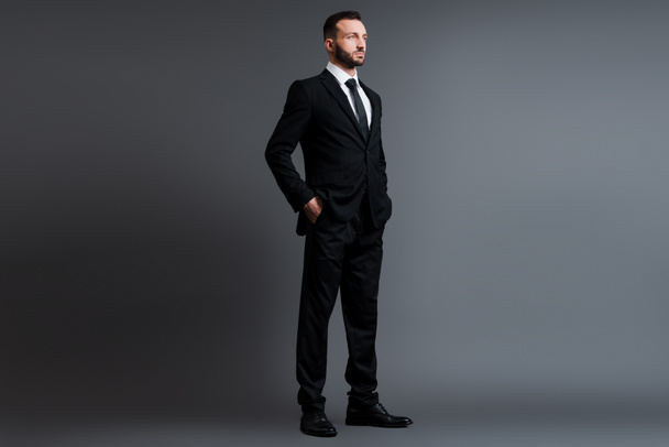 schöner Geschäftsmann im Anzug mit Händen in Taschen auf grau  - Foto, Bild