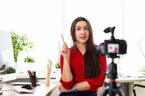 Jeune femme assise au bureau en face de la caméra et présentant des services
 - Photo, image