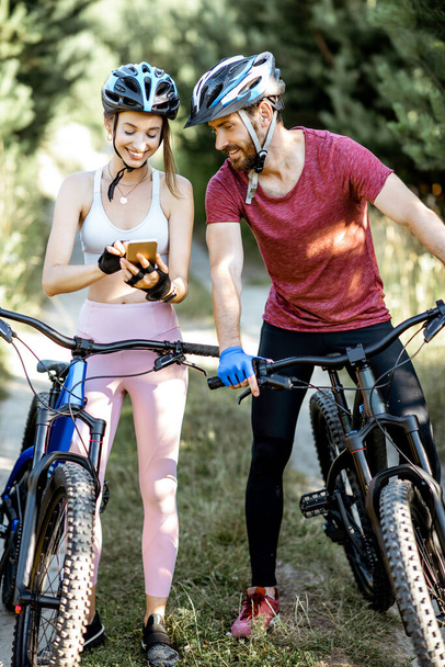 Hombre y mujer ciclistas con smartphone en la carretera forestal
 - Foto, imagen