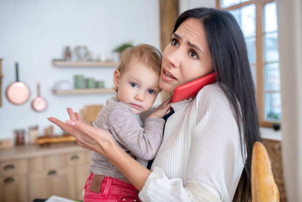 Mamá trabajadora sosteniendo al bebé, hablando por teléfono, sintiéndose angustiada
 - Foto, imagen