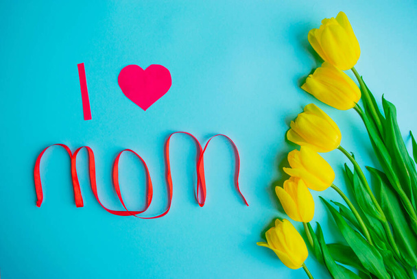 Happy Mother's day card. Creative holiday greeting card with the bouquet of beautiful spring yellow tulips flowers on the light blue background. Mothers day flat lay concept. Still life, top view. - Fotó, kép