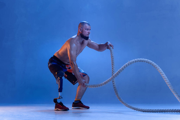 Athlete disabled amputee isolated on blue studio background - Foto, imagen