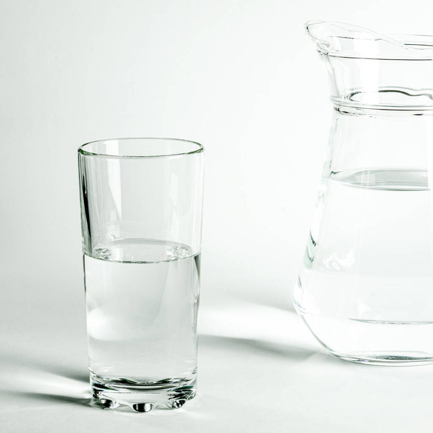 L'acqua limpida pura in un bicchiere e una brocca sta su uno sfondo bianco. isolato - Foto, immagini