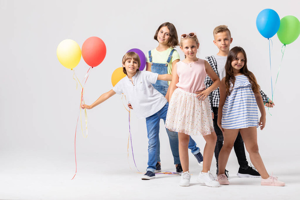 Group of happy children is standing together in a white room and holding colorful balloons - 写真・画像