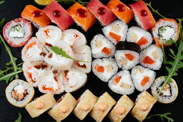 set di involtini di sushi con salmone, gamberetti e anguilla affumicata con crema di formaggio su piatto nero
 - Foto, immagini