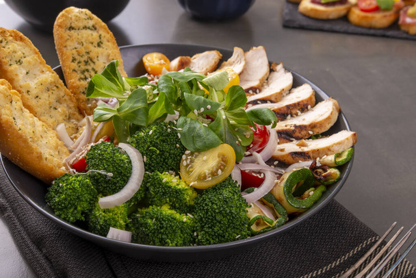 Salad of grilled chicken breast with broccoli, tomatoes and lamb's lettuce on a dark table. Variety of Caesar salad - Photo, Image