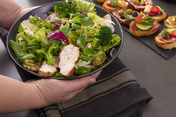 Kädet tarjoillaan lautasella grillattua kanaa, salaattia ja parsakaalisalaattia
 - Valokuva, kuva