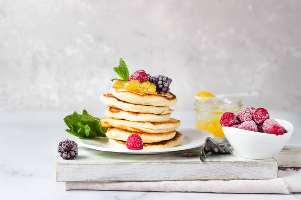Homemade pancakes with jam, frozen raspberries and blackberries and mint on wooden cutting board. Light grey background. Breakfast.  - Foto, Imagen