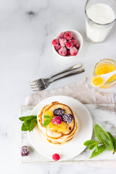 Homemade pancakes with jam, frozen raspberries, blackberries and mint and glass with milk on light grey background. Perfect idea for breakfast or snack. Top view.  - Foto, Imagem